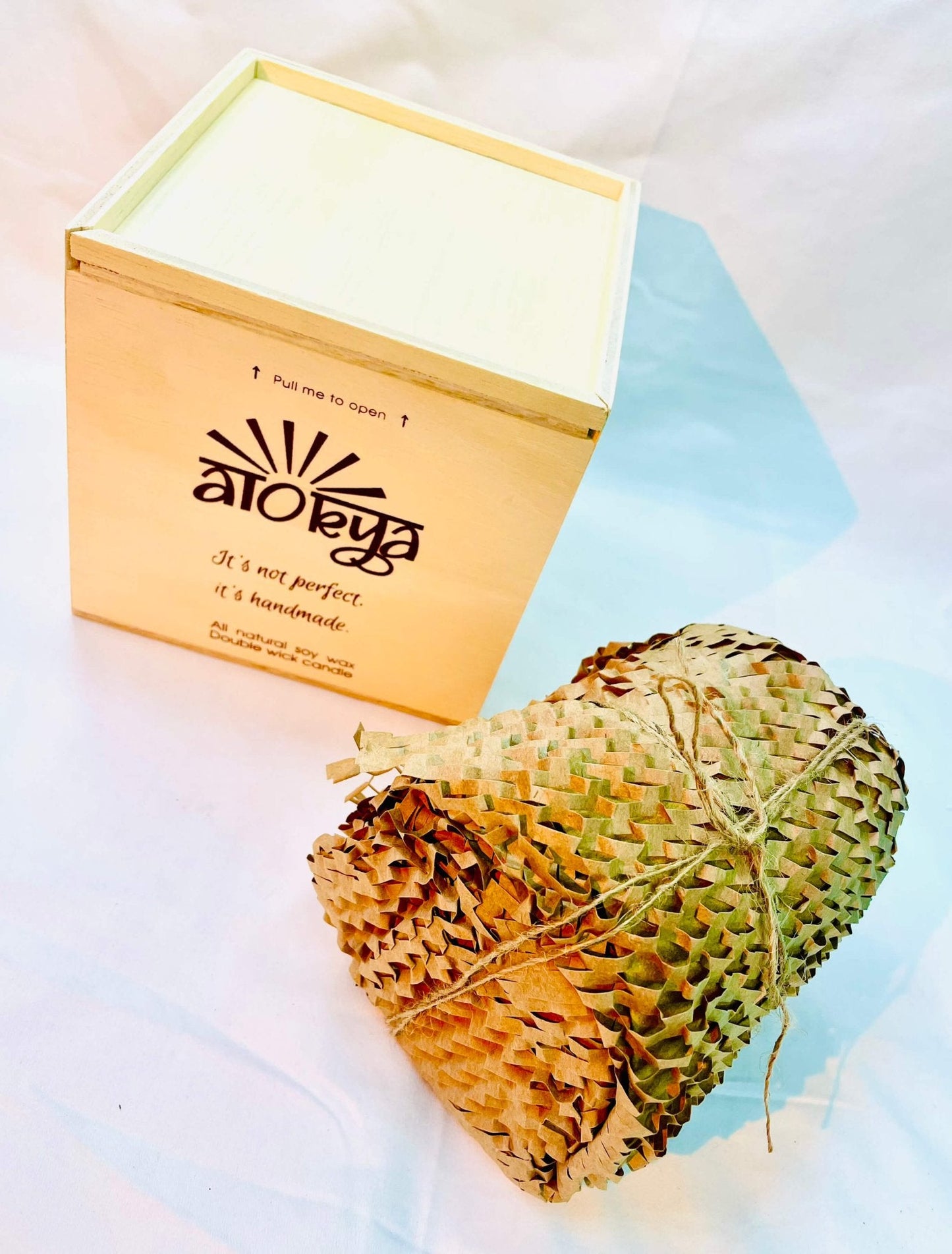 100% natural soy wax scented candle wrapped in honeycomb paper near a wood candle box.