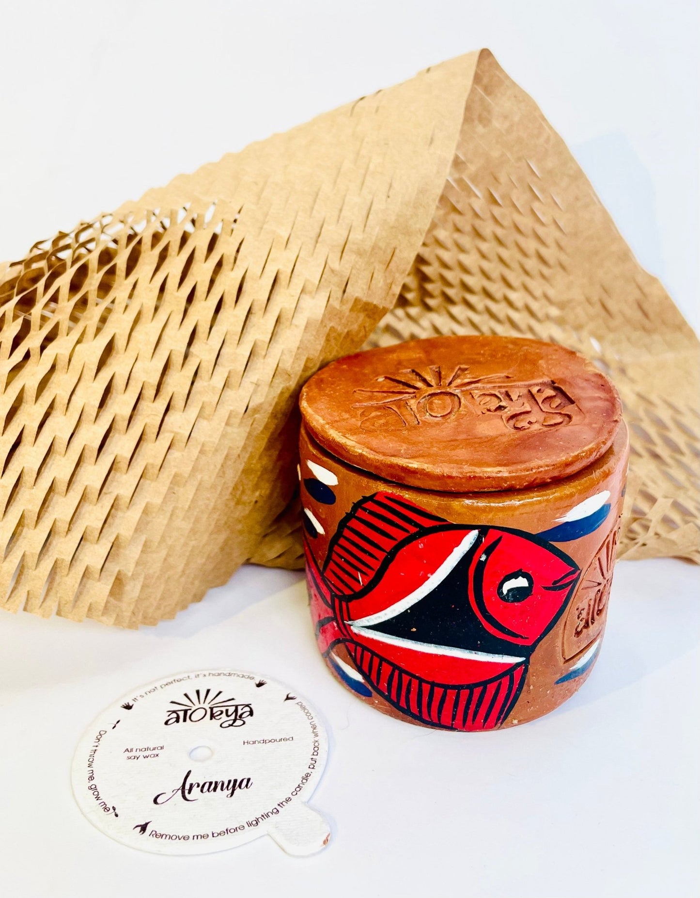 100% natural soy wax scented candle in a terracotta jar hand-painted with a red coloured fish is covered with a terracotta clay candle snuffer while honeycomb paper and seed paper candle dust cover is placed around the candle