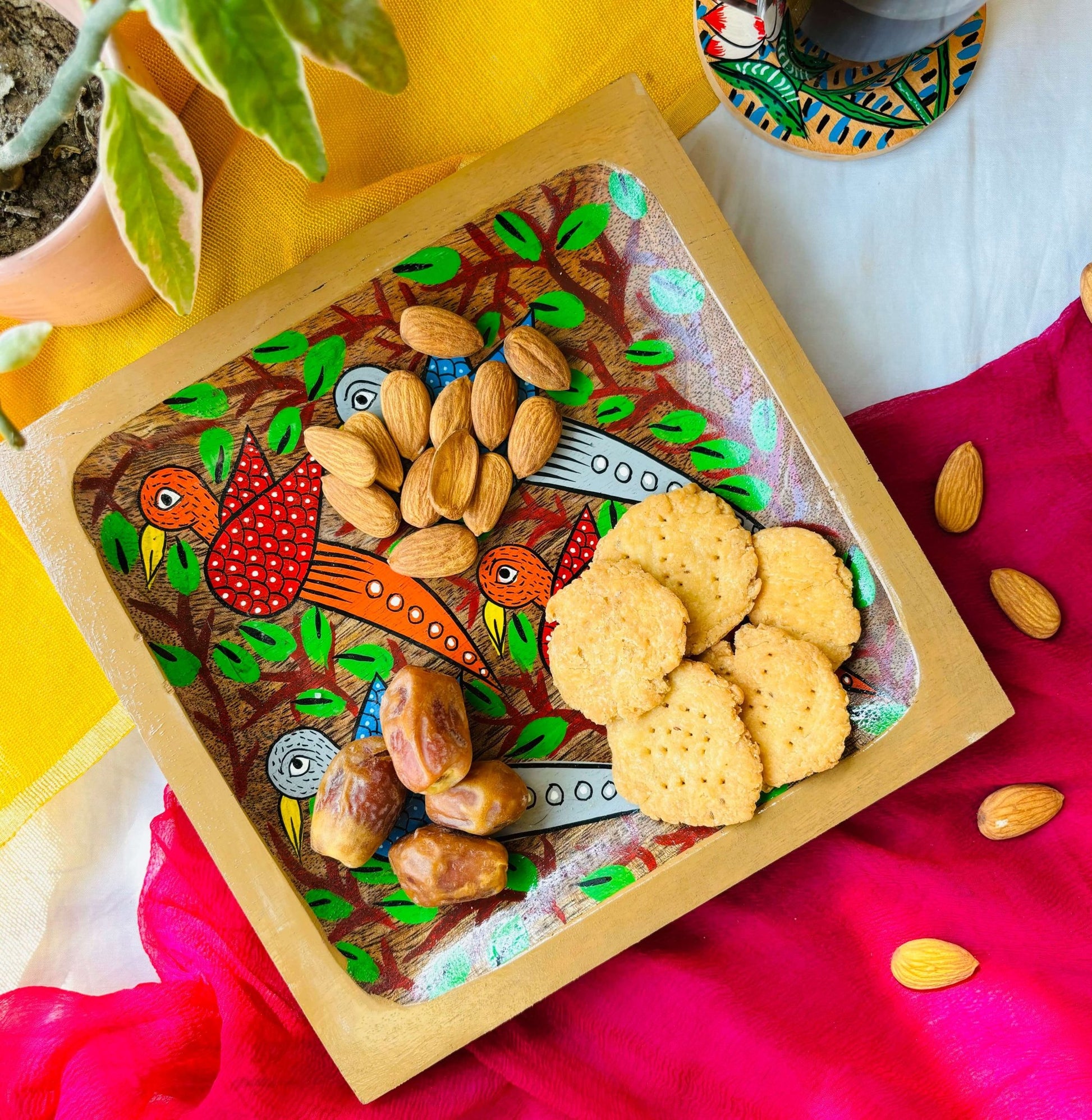 Biscuits, almonds and dates served in a handcrafted pure mango wood square wood tray, painted with two red birds, two blue birds and tea branches by generational Pattachitra artists