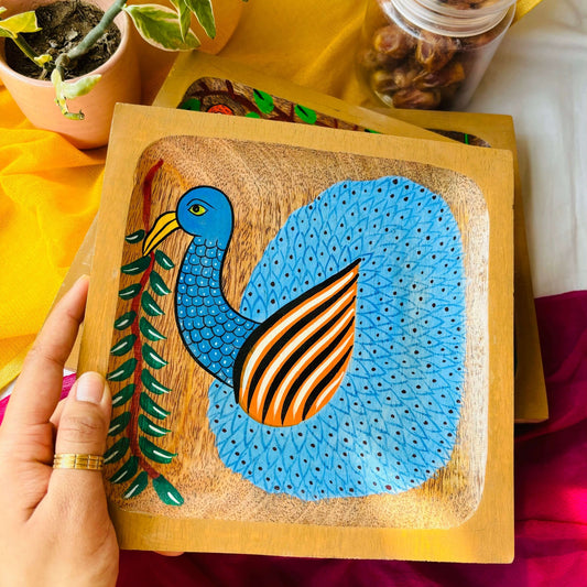 A hand holding square wood tray or trinket tray handcrafted from mango wood and featuring peacock motif, hand painted by the generational Pattachitra artists of Pingla