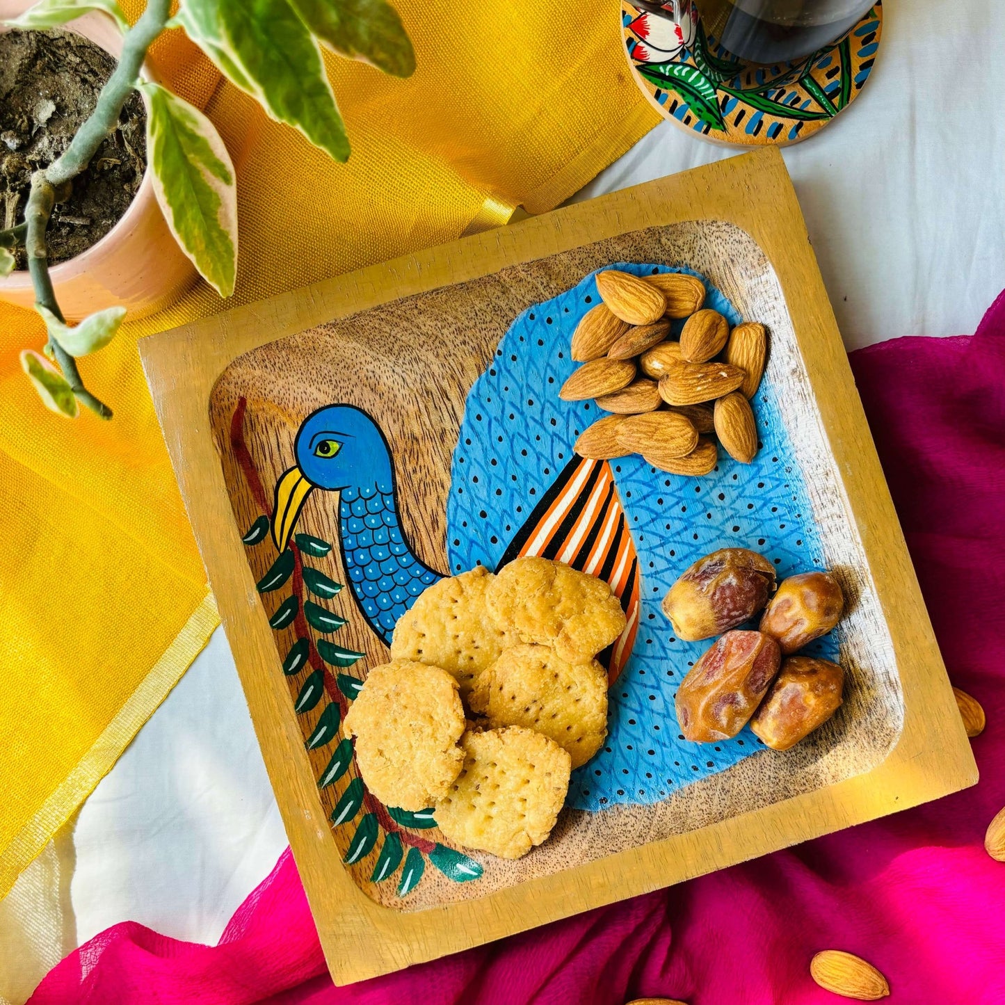 Biscuits, dates and almonds are served in a handcrafted mango wood square wood tray or a trinket tray, painted with a peacock by generational Pattachitra artists