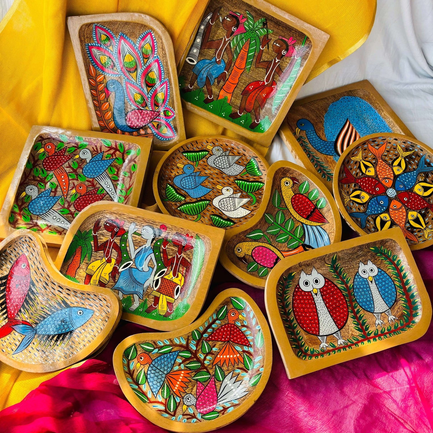 Three round wooden tea trays, two square wood trays, three rectangular wooden trays and three moon-shaped wooden serving trays or trinket trays featuring Indian folk art, West Bengal Pattachitra paintings of four birds, two peacocks, two fish, one owl, and two tribal motifs, inspired from Indian folklore
