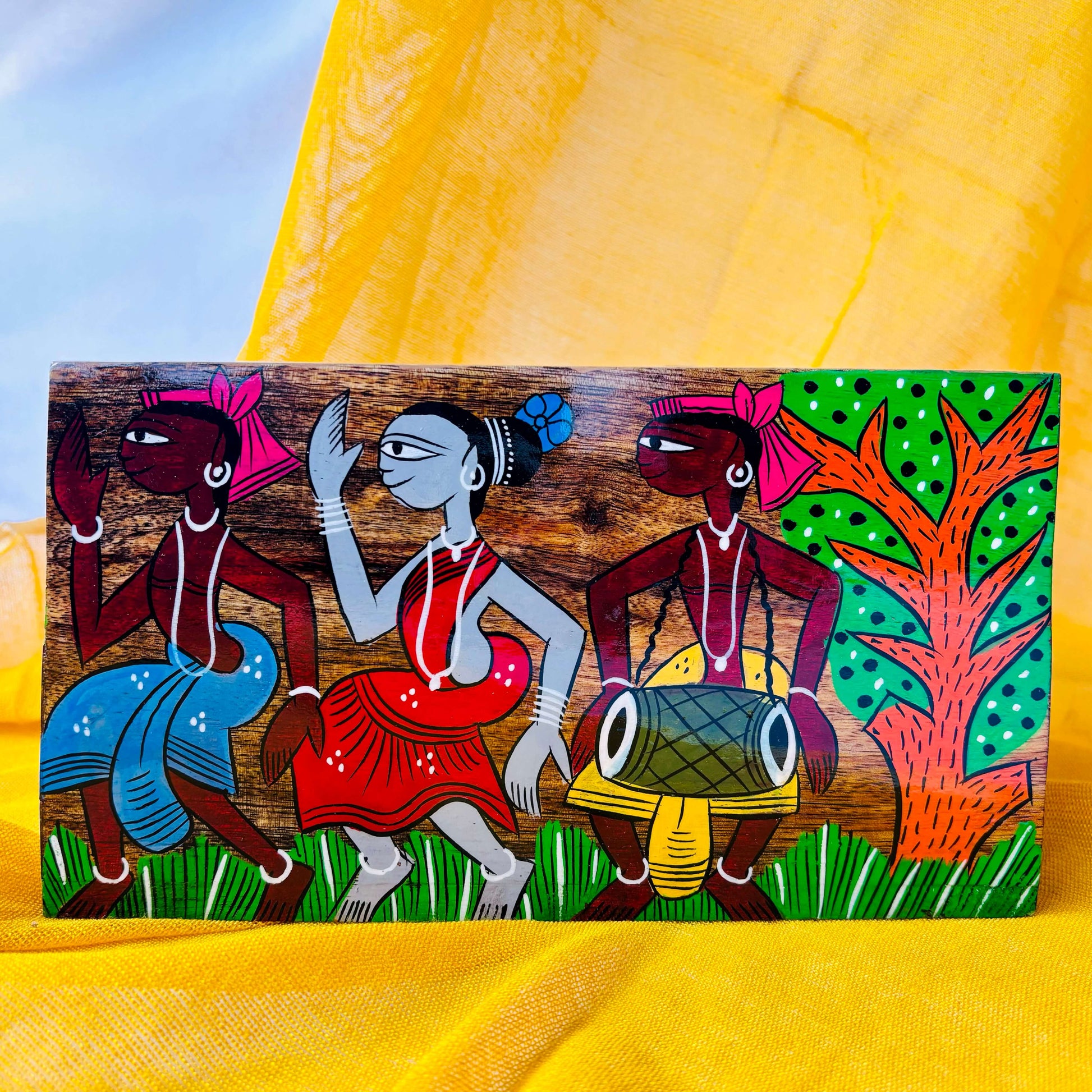 A pure mango wood table organiser or wood cutlery holder in a yellow background, painted with a scene of tribal celebration, where two people are dancing and one is playing a musical instrument surrounded by trees.