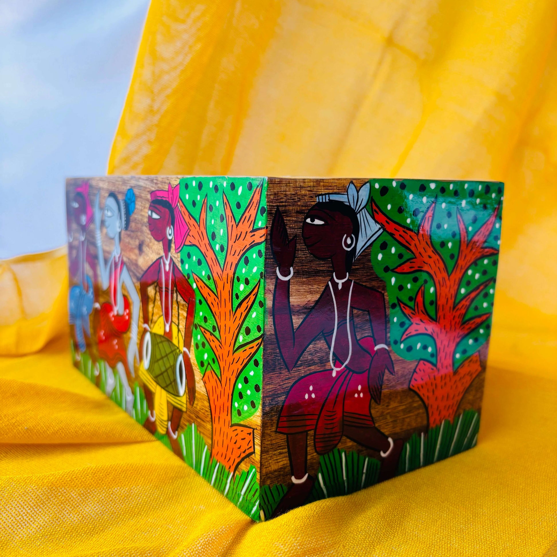 A pure mango wood table organiser or wood cutlery holder, with a painting of a tribal celebration where three people are dancing and one person is playing a musical instrument surrounded by trees.