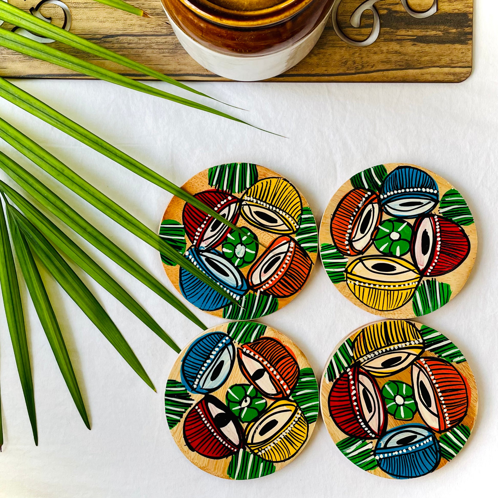 Four pure mango wood round wooden coasters, with a painting of four tabla, a type of Indian classical musical instrument in each wood coaster