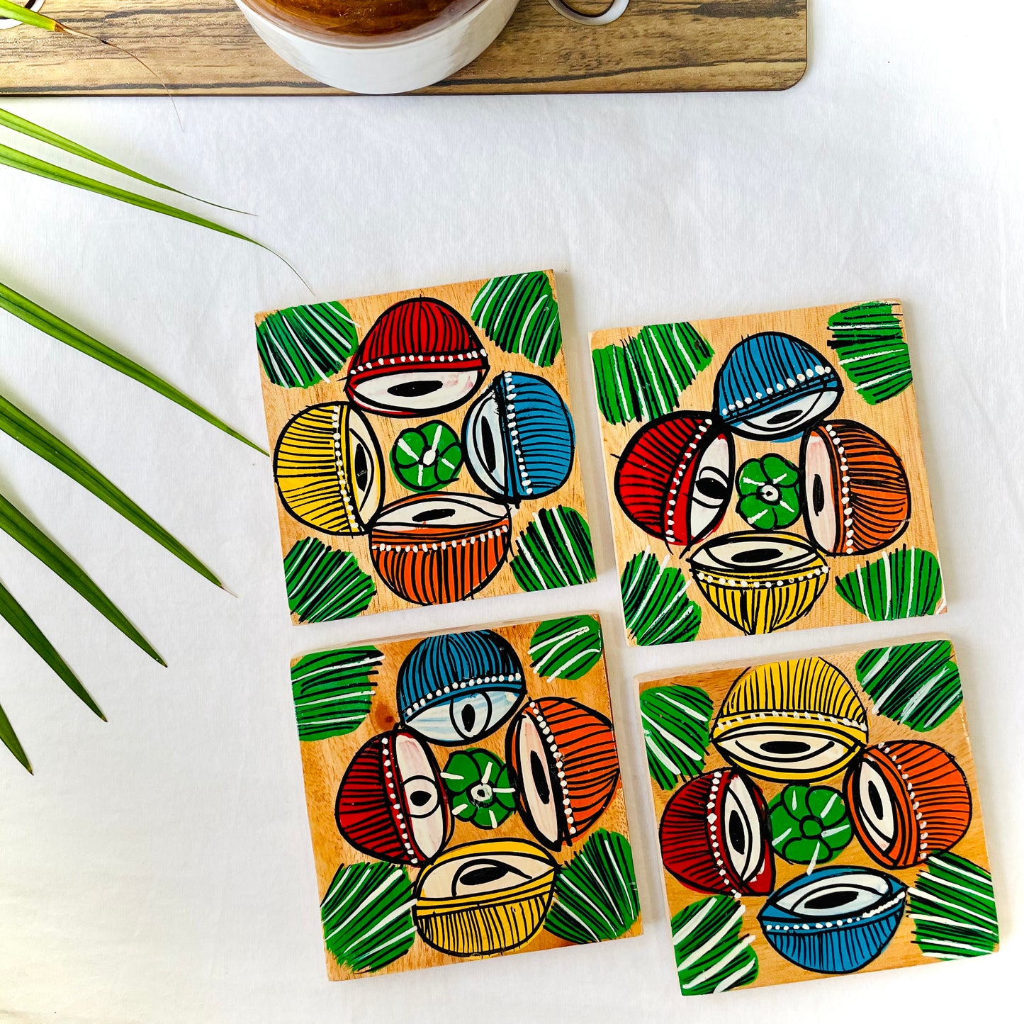 Four pure mango wood square wooden coasters, with a painting of four tabla, a type of Indian classical musical instrument in each wood coaster