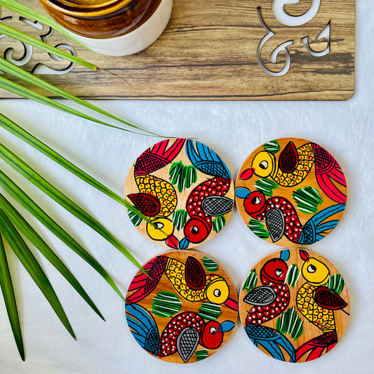 Four pure mango wood round wooden coasters, with a painting of one yellow bird with red feathers and a beak and one red with blue feathers and a beak along with some leaf in each wood coaster