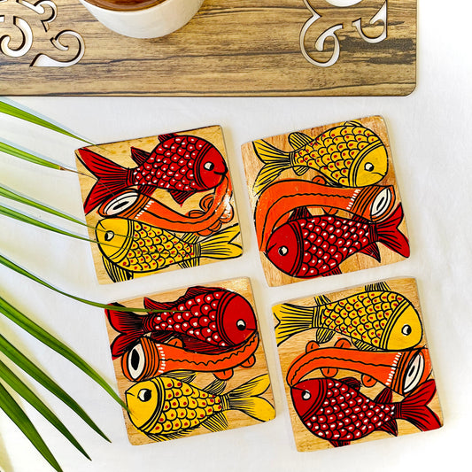 Four pure mango wood square wooden coasters, with a painting of one yellow fish and one redfish along with an Indian classical musical instrument in each wood coaster
