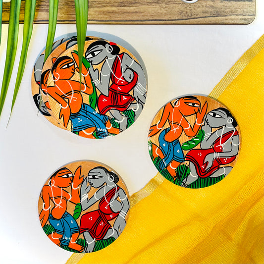 Three pure mango wood round wooden coasters, hand painted with tribal characters dancing placed against a yellow backdrop and leaves in the background