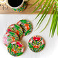 Five pure mango wood round wood coasters painted with four lotus with leaves and water in each wood coaster are placed near a teacup filled with black tea with leaves in the background