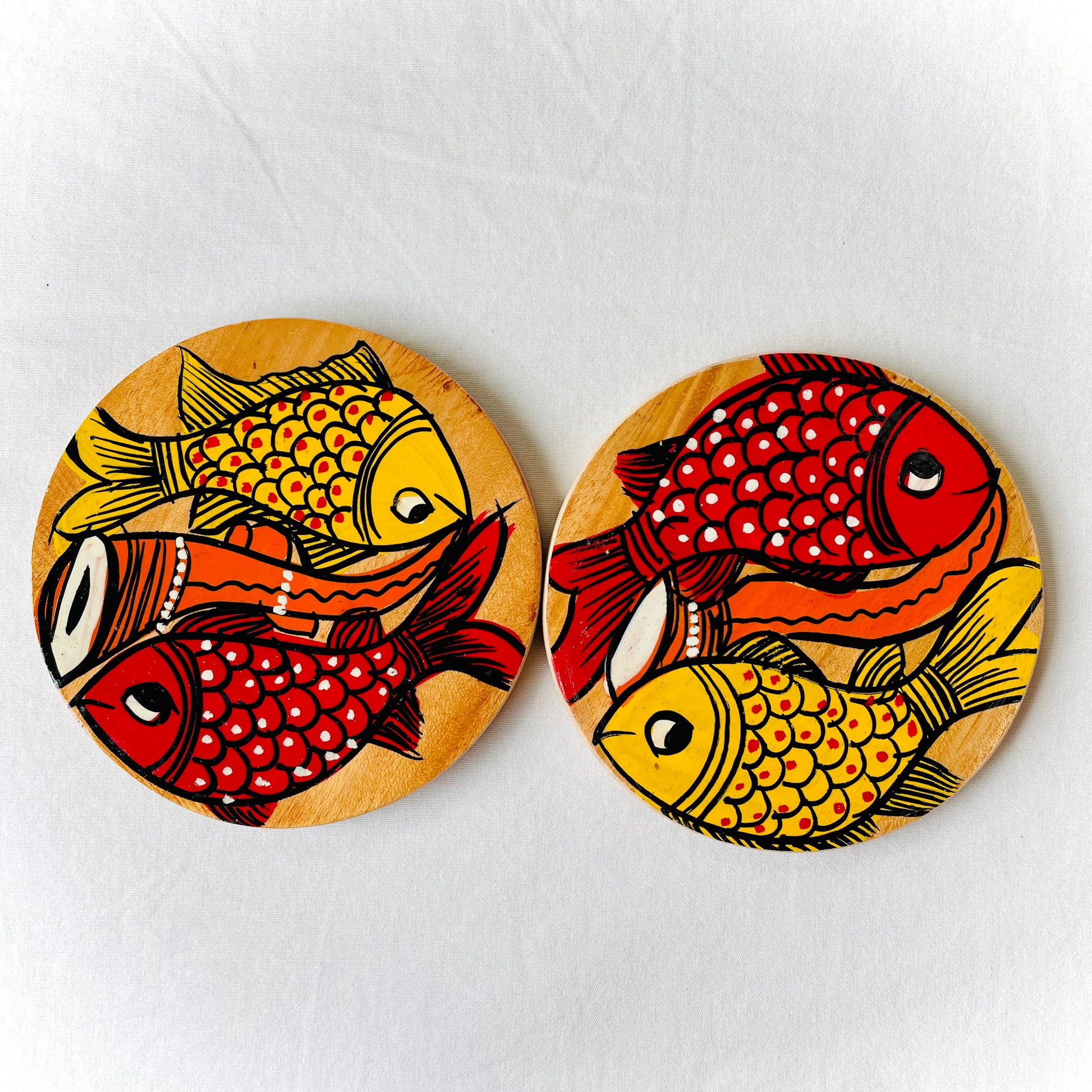 Two round wood coasters displayed against a white background, feature one yellow fish and one redfish along with an Indian classical musical instrument in each wood coaster