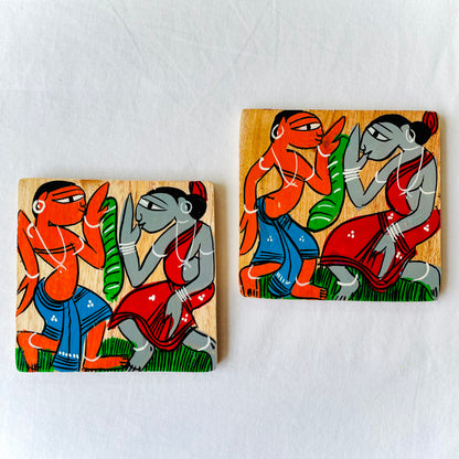Two square wood coasters displayed against a white background feature two tribal characters dancing
