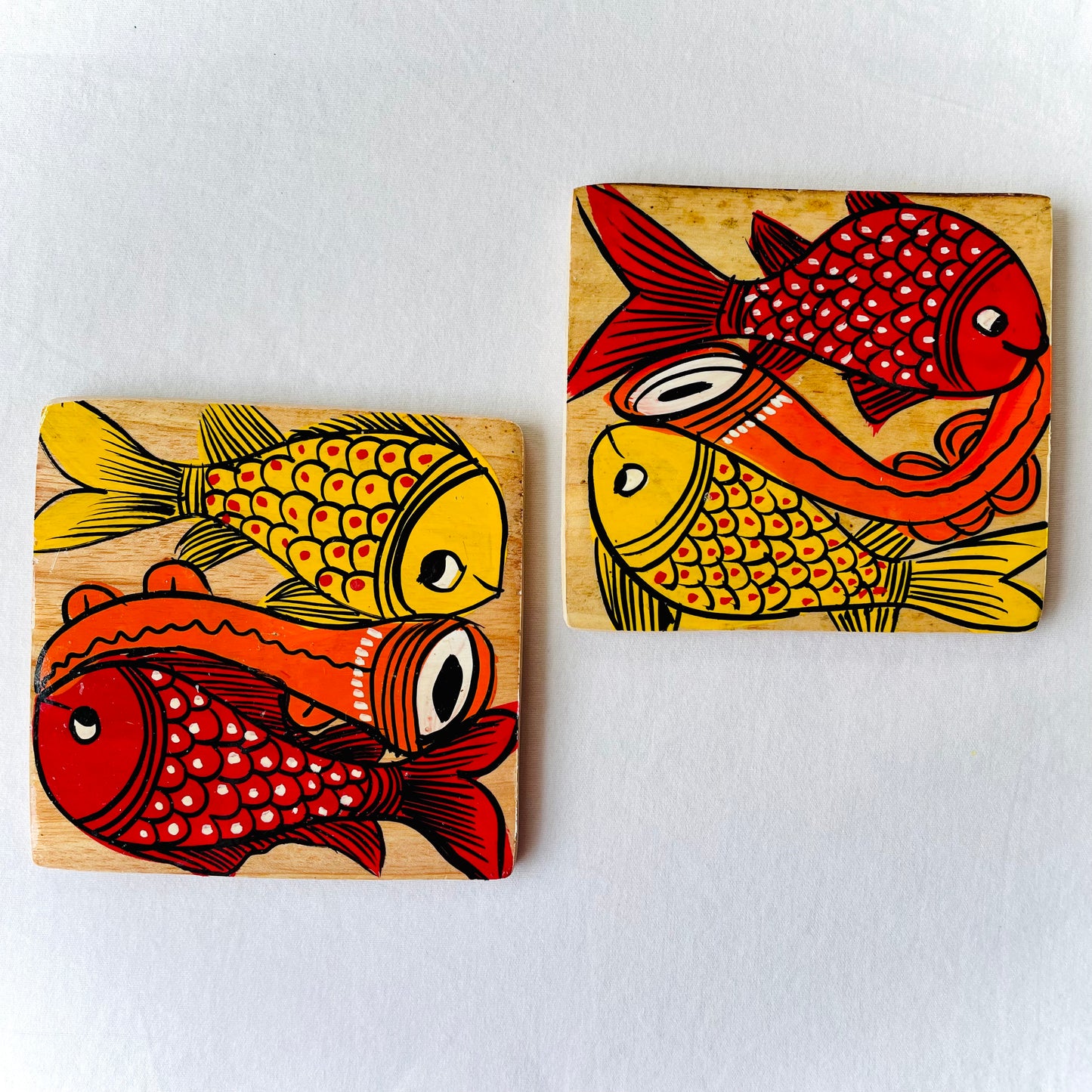 Two square wood coasters displayed against a white background, feature one yellow fish and one redfish along with an Indian classical musical instrument in each wood coaster