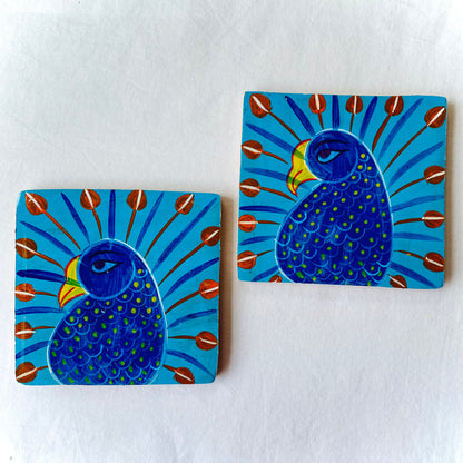 Two coaster image: Two square wood coasters displayed against a white background, feature two peacocks with blue bodies, red feathers and yellow beaks