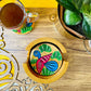 bird print round wooden coaster placed in a round wooden coaster holder near a flower pot and tea cup placed on a round wooden coaster.