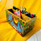 An aerial view of three pens, two scissors, six coloured pens and a bookmark placed in a 9”x5”x3” pure mango wood table organiser or wood cutlery holder wooden tissue holder with 3 small and one large compartment, handcrafted by rural artisans and painted with an elephant, tree branches and leaves motifs.