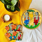 One hand-woven bamboo fruit box, a set of four square wood coasters hand painted with a motif of tribal characters, and a double wick scented candle, displayed against a yellow background with a plant pot beside them