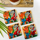 Four pure mango wood square wooden coasters, with a painting of two tribal people dancing at a wedding, are placed near a brown woodboard