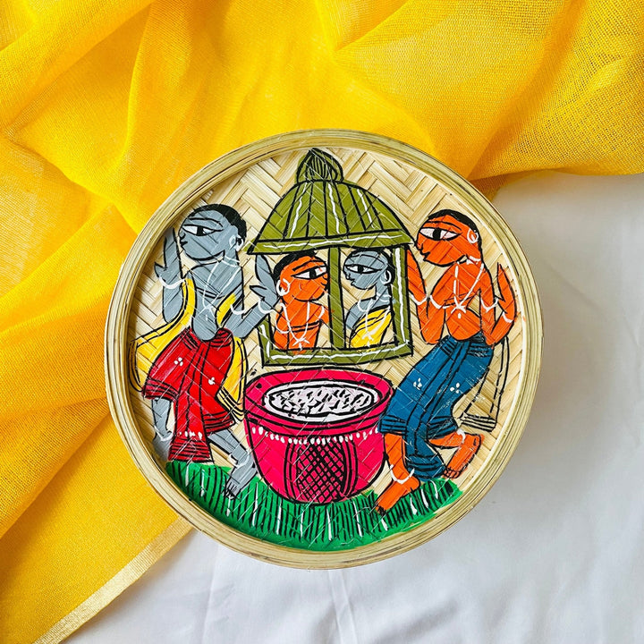 A handwoven bamboo utility and fruit box hand-painted with tribal characters indulged in a wedding celebration is displayed against a yellow background