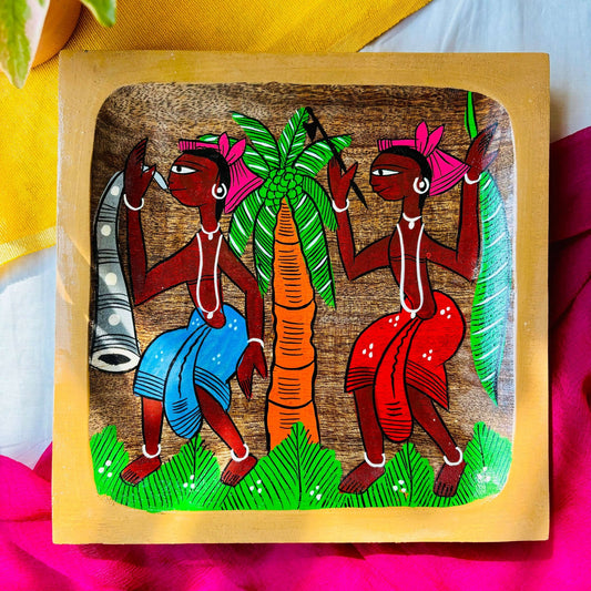 Pure mango wood square wood serving tray/trinket tray hand painted with two tribal men wearing blue and orange clothes and a coconut tree is displayed against a yellow and pink background