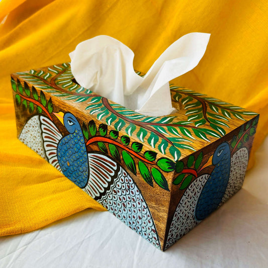A pure mango wood wooden tissue holder, with peacock, tree branches and leaves hand painted on it, placed at an angle with a yellow background