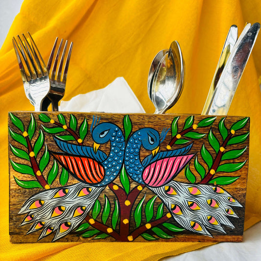 Three spoons, three forks and three knives organised in a pure mango wood cutlery holder showcasing pattachitra painting of two peacocks surrounded by tree branches and leaves