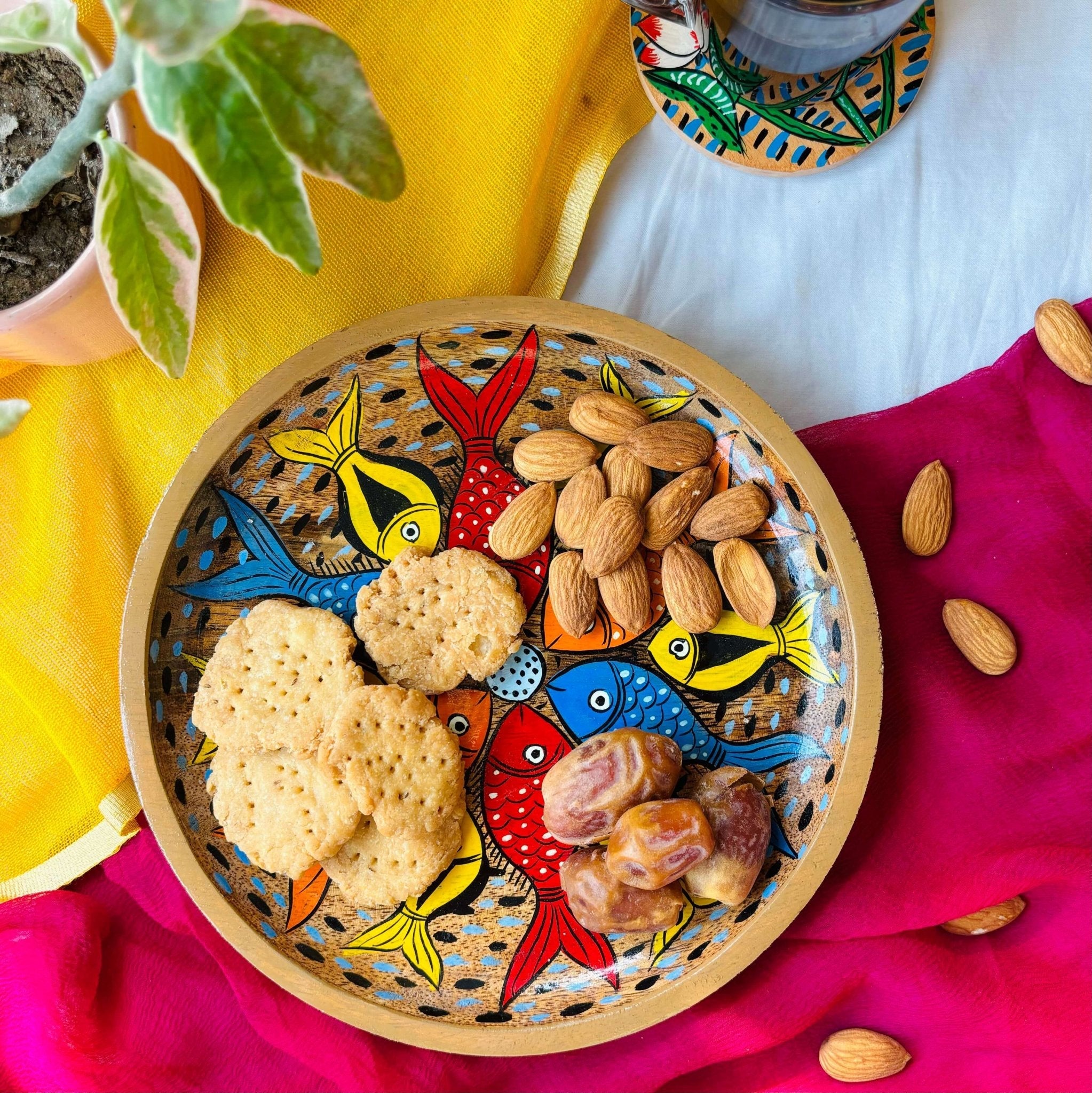 Biscuits, dates and almonds are served in a handcrafted mango wood round wooden tray or a trinket tray, painted with fish motifs by generational Pattachitra artists