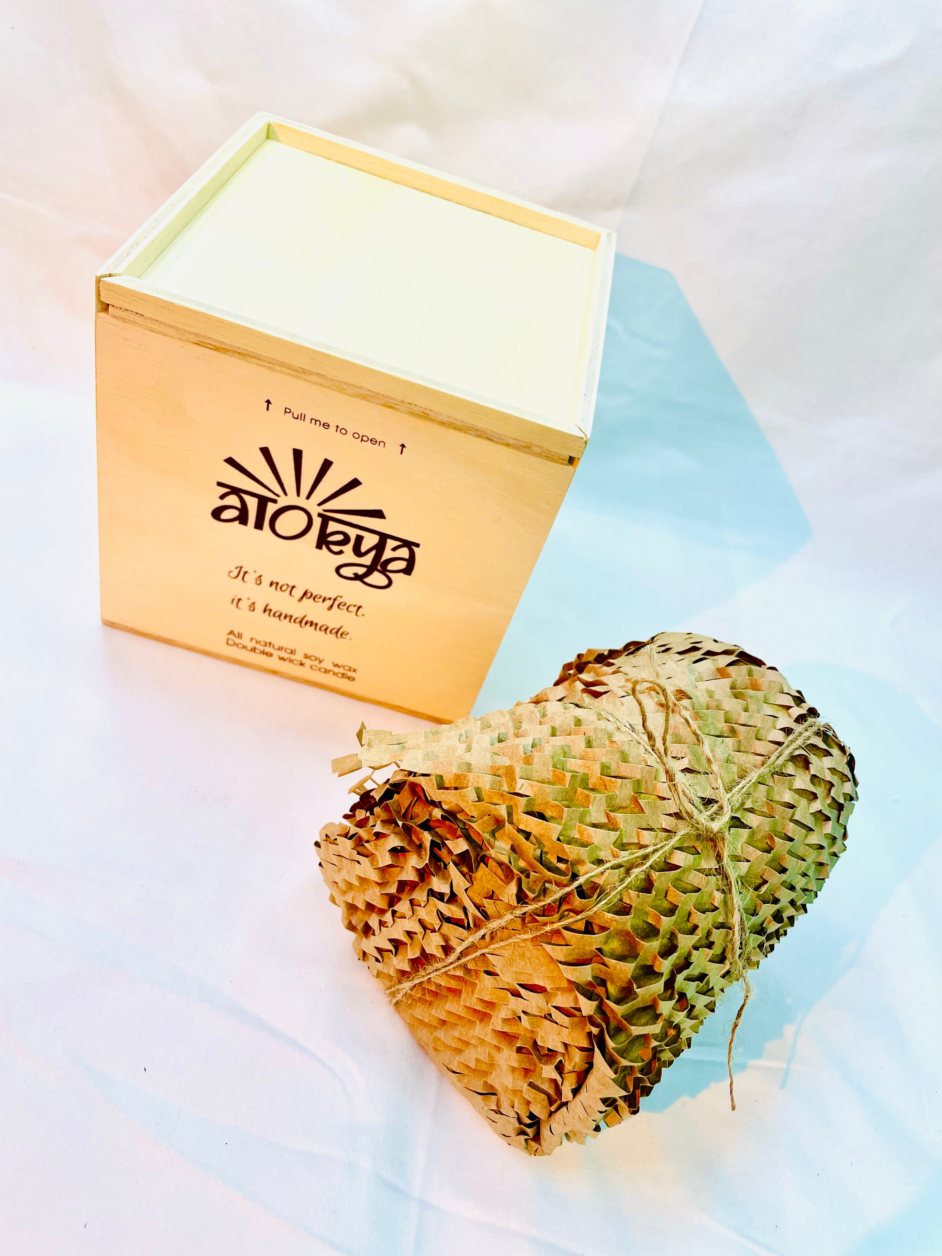 100% natural soy wax scented candle wrapped in honeycomb paper near a wood candle box.