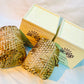 Two 100% natural soy wax scented candles wrapped in honeycomb paper are placed near two brown wood boxes.