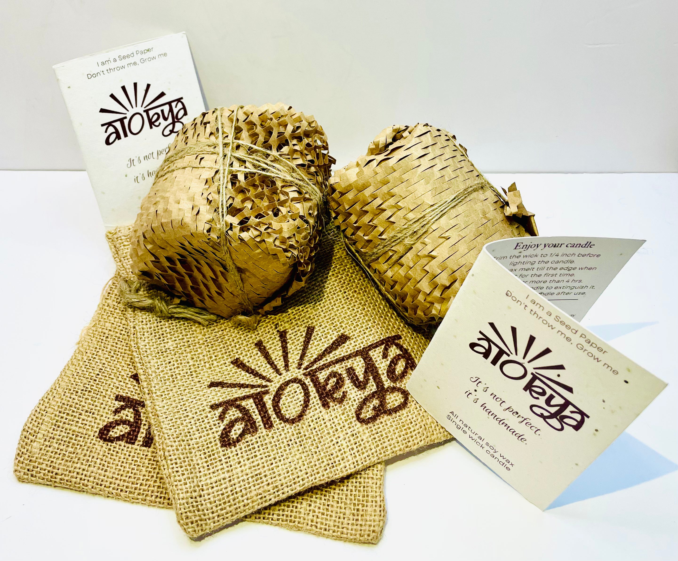 Two 100% natural soy wax scented candles wrapped in honeycomb paper are placed near two seed paper information cards and two brown jute bags.