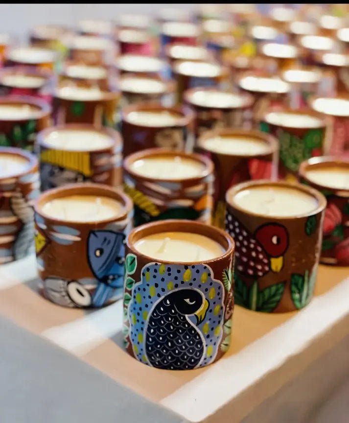 100% natural soy wax scented candles in terracotta jars with paintings of birds, peacocks and fish are displayed on a table covered with white cloth.