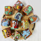 11 natural soy wax scented candles in terracotta jars hand-painted with bird, fish, peacock, owl, elephant, and tribal motifs are placed on a wooden tray with handles