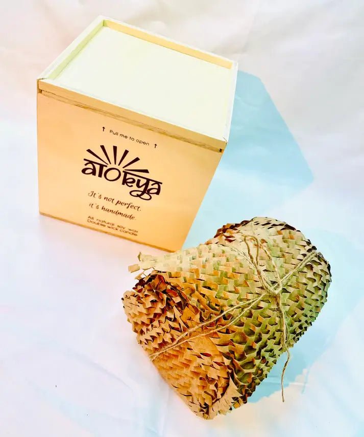 100% natural soy wax scented candle wrapped in honeycomb paper near a wood candle box.