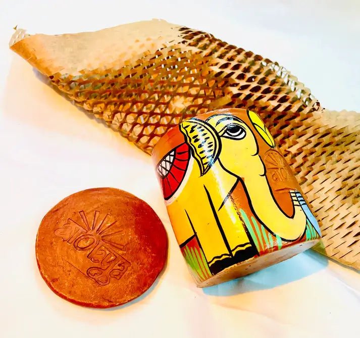 100% natural soy wax scented candle in a terracotta jar, hand painted with yellow elephant, is placed near terracotta clay candle snuffers and honeycomb paper.