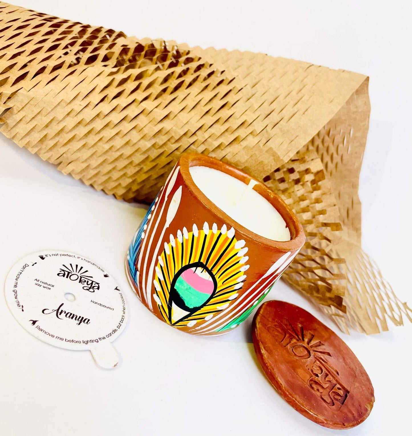 100% natural soy wax scented candle in a terracotta jar hand painted with yellow feathers having a seed paper candle dust cover, honeycomb paper and candle snuffer placed around the candle