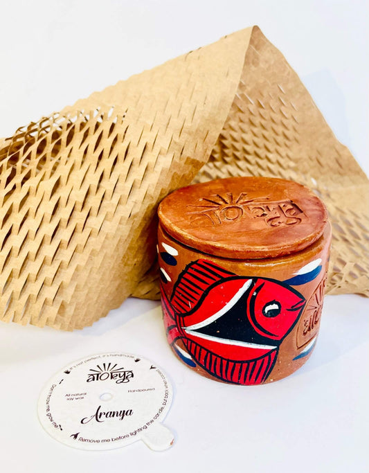 100% natural soy wax scented candle in a terracotta jar hand-painted with red and black fish is covered with terracotta clay candle snuffer and a seed paper candle dust cover and honeycomb paper are placed around the candle
