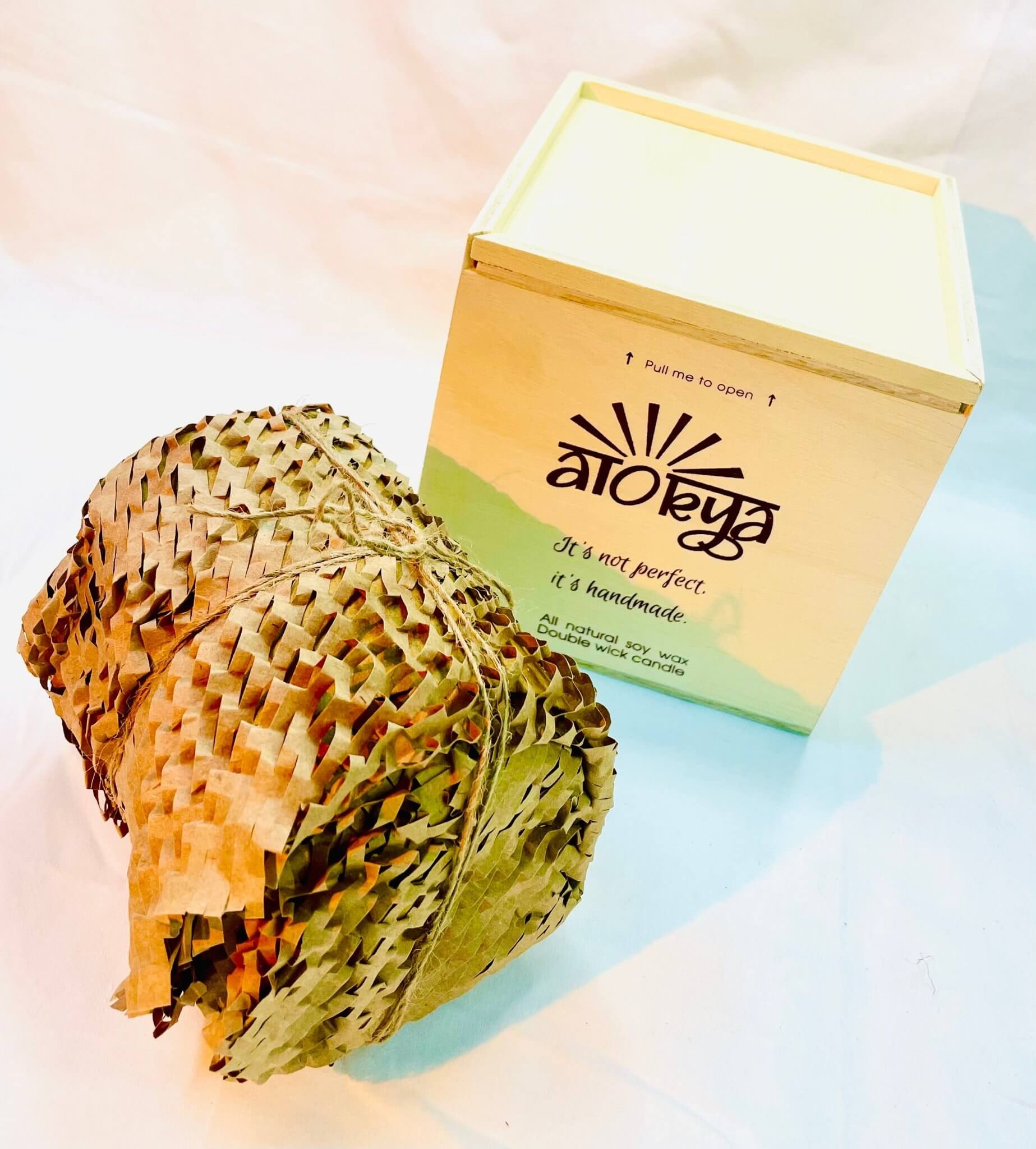 100% natural soy wax scented candle wrapped in honeycomb paper near a wood candle box.