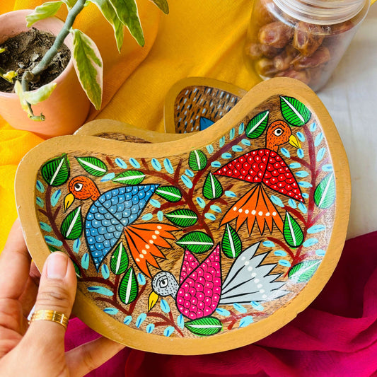A hand holding a moon-shaped wooden platter and trinket tray handcrafted from mango wood and featuring three bird paintings, hand painted by the generational Pattachitra artists of Pingla