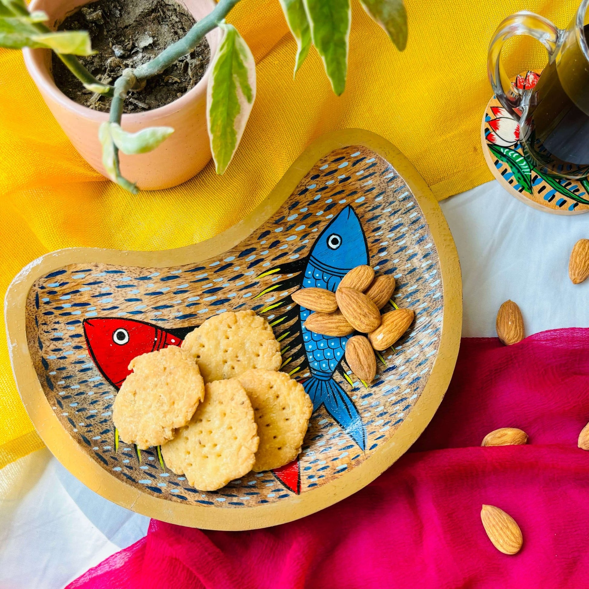 Biscuits and almonds are served in a handcrafted mango wood moon-shaped wooden tray for the kitchen, painted with two fishes by generational Pattachitra artists