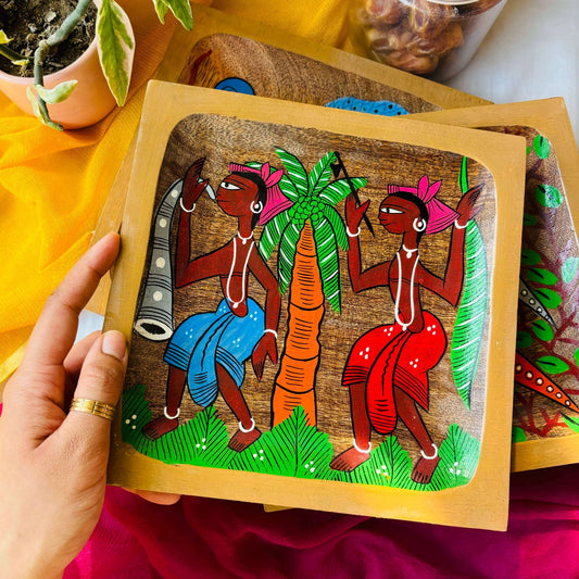 A hand holding square wood tray or trinket tray handcrafted from mango wood and featuring tribal painting, hand painted by the generational Pattachitra artists of Pingla