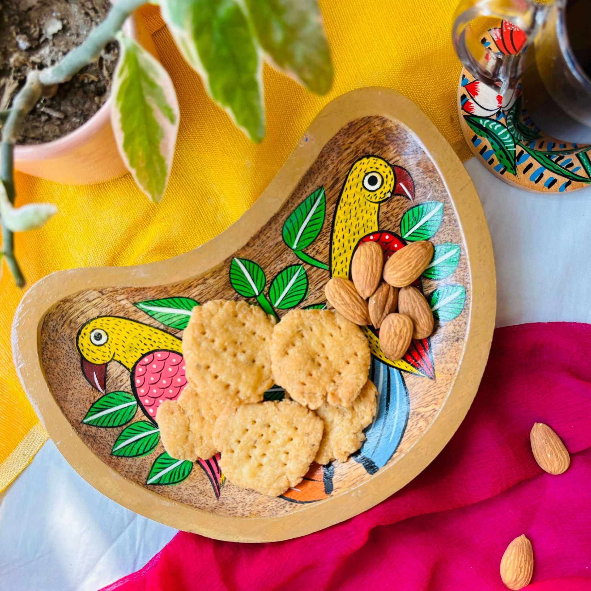 Biscuits and almonds are served in a handcrafted mango wood moon-shaped wooden tray for the kitchen or trinket tray, painted with a bird couple painting by generational Pattachitra artists.