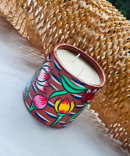100% natural soy wax scented candle in a terracotta jar, hand painted with four lotus motifs, is placed near a honeycomb paper