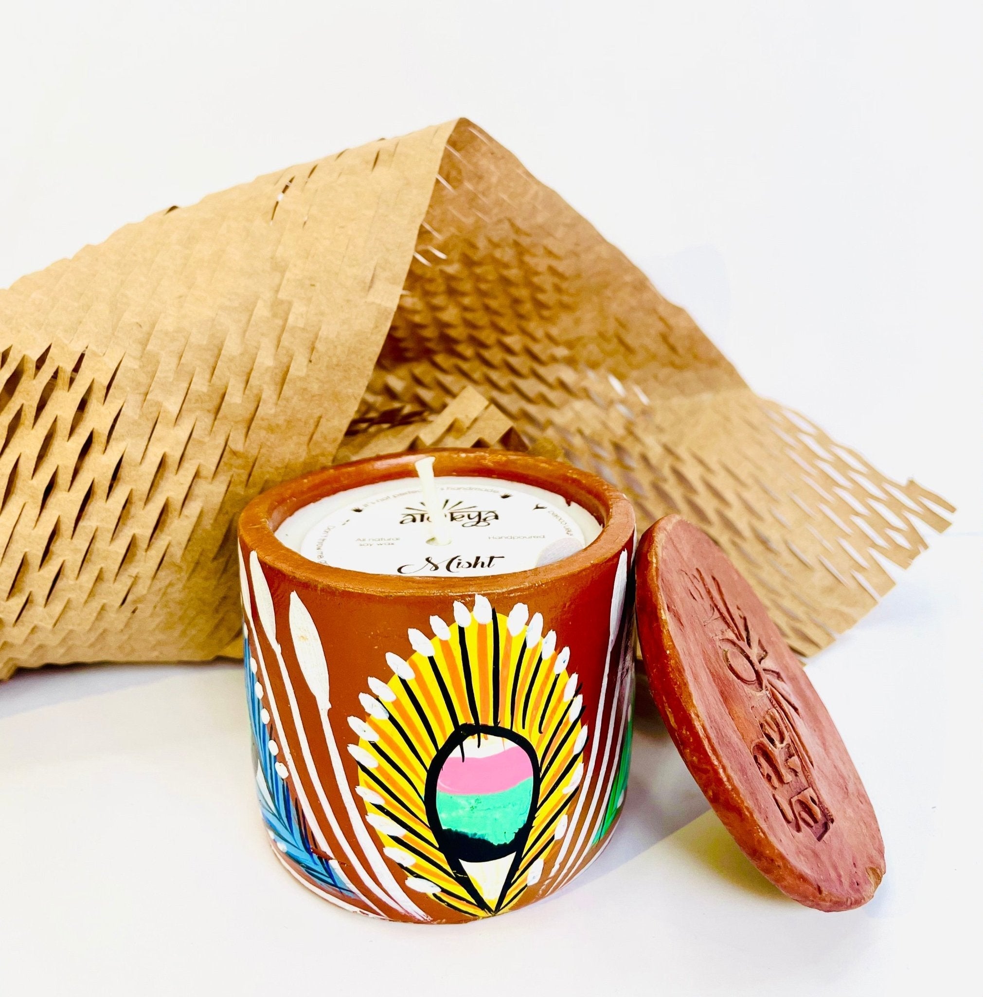 100% natural soy wax scented candle in a terracotta jar hand painted with yellow feathers is covered with a seed paper candle dust cover and honeycomb paper and candle snuffer is placed around the candle