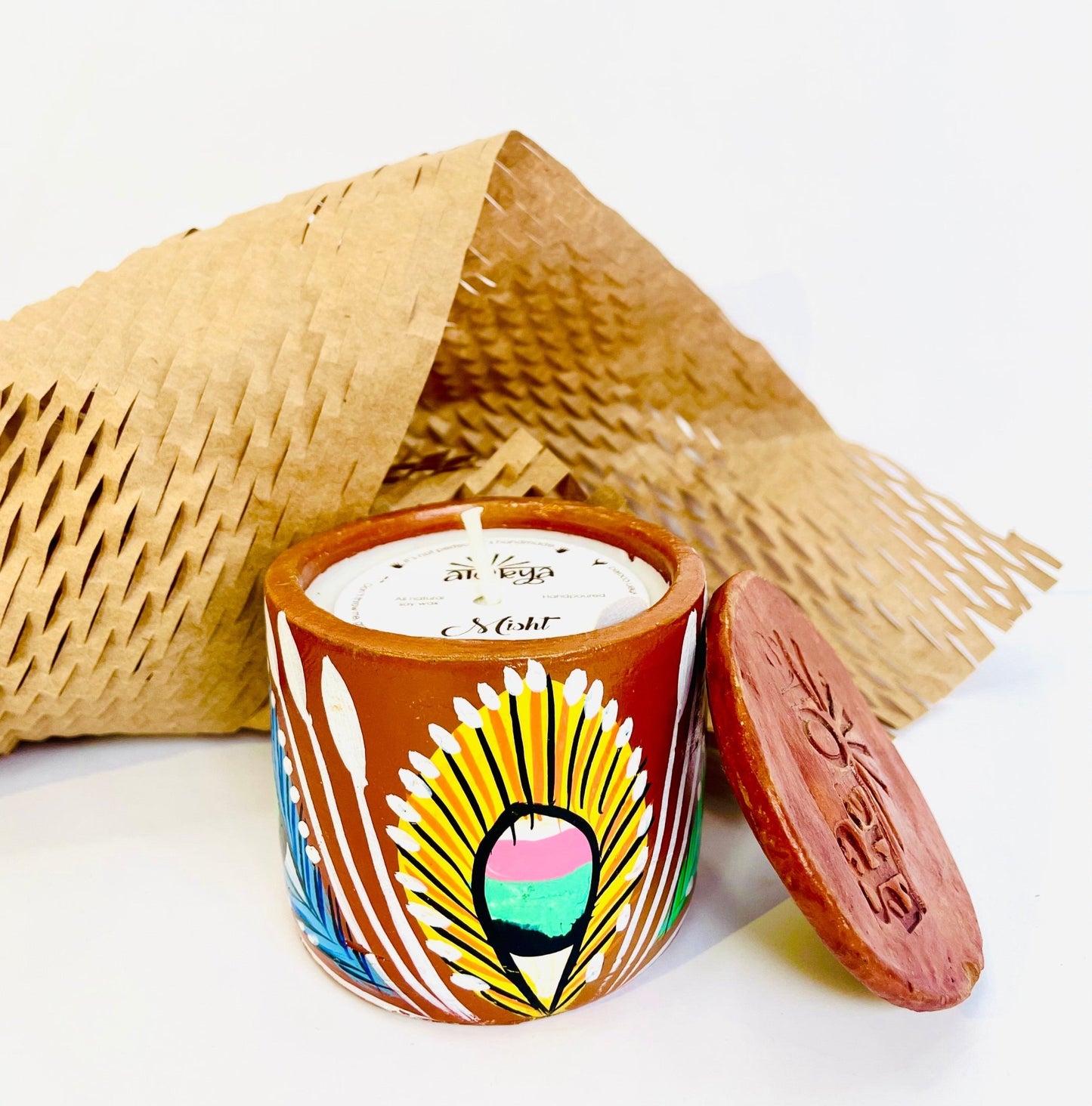 100% natural soy wax scented candle in a terracotta jar hand-painted with yellow feathers is covered with a seed paper candle dust cover while honeycomb paper and candle snuffer are placed around the candle