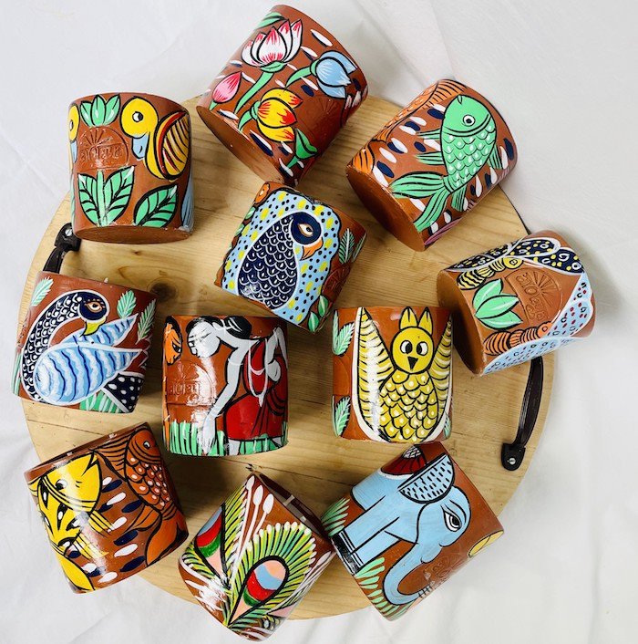 11 natural soy wax scented candles in terracotta jars hand-painted with bird, fish, peacock, owl, elephant, and tribal motifs are placed on a wooden tray with handles