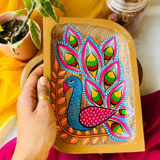 Hand holding rectangular wooden tray or trinket tray handcrafted from mango wood and featuring peacock motif, hand painted by the generational Pattachitra artists of Pingla