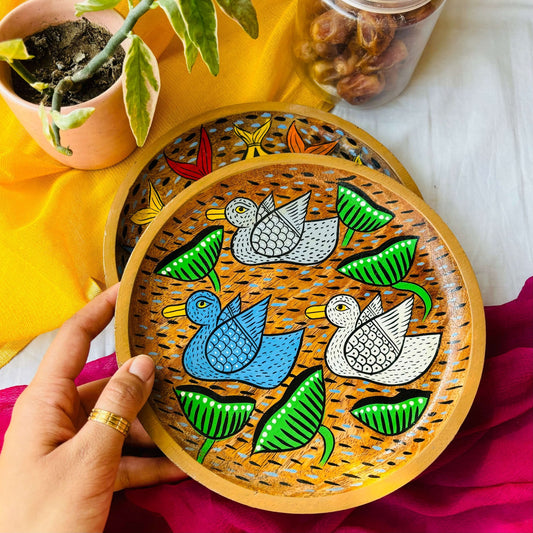 Hand holding round wooden tray or trinket tray handcrafted from mango wood and featuring three bird motifs, hand painted by the generational Pattachitra artists of Pingla