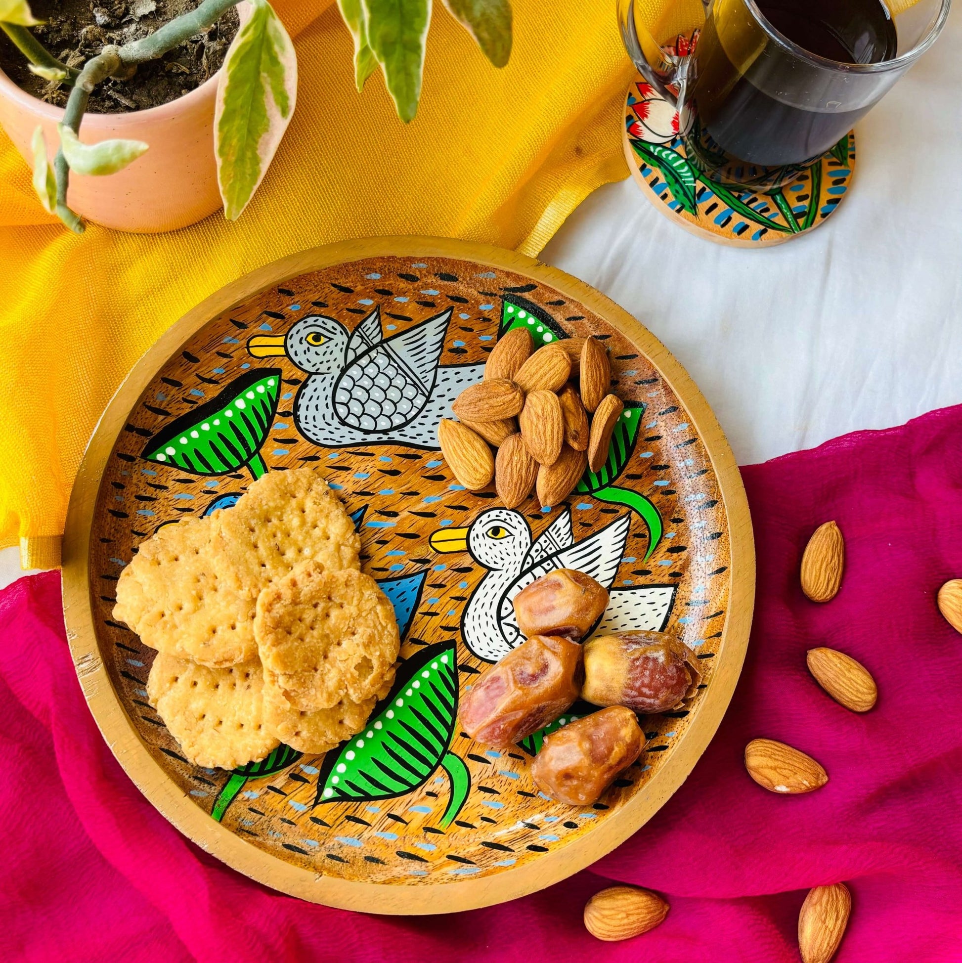 Biscuits, dates and almonds are served in a handcrafted mango wood round wooden tray or a trinket tray, painted with three birds by generational Pattachitra artists