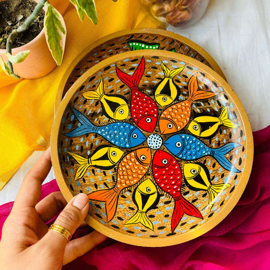 Hand holding round wooden tray or trinket tray handcrafted from mango wood and featuring fish motifs, hand painted by the generational Pattachitra artists of Pingla
